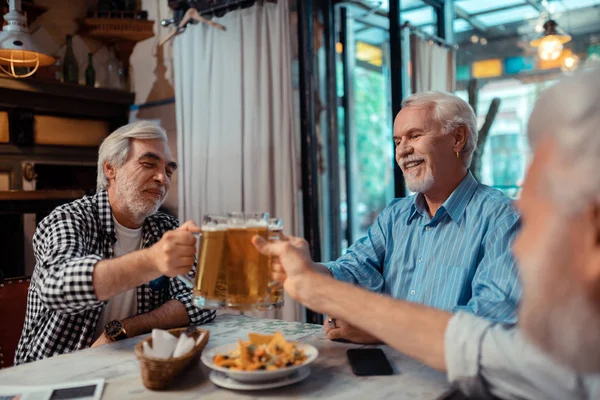 Emerytowany szaro-włosy mężczyźni jedzą przekąski i picie piwa — Zdjęcie stockowe