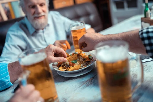 Uomini maturi che prendono nachos mentre bevono birra — Foto Stock