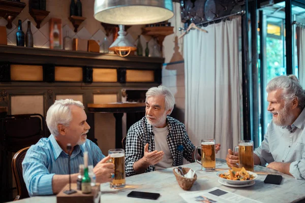 Tři penzisté jedí nachos a pijí pivo — Stock fotografie