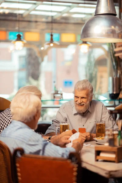 Весёлые пенсионеры вместе играют в карты в пабе — стоковое фото