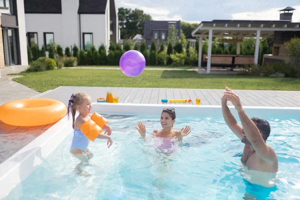 Menina sentindo-se feliz enquanto joga bola com os pais na piscina — Fotografia de Stock