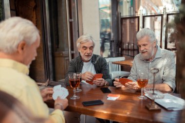 Retired men playing cards and drinking alcohol outside clipart