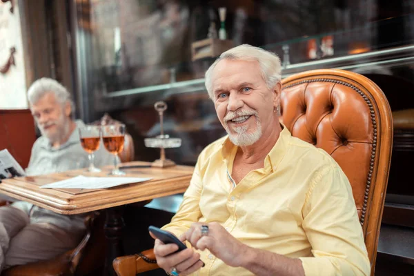 Blue-eyed man holding phone while spending time with friend — Stock Photo, Image