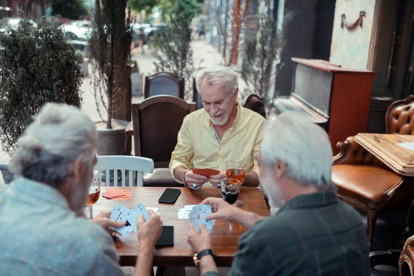 Retired man sitting outside pub and playing cards — Stock Photo, Image