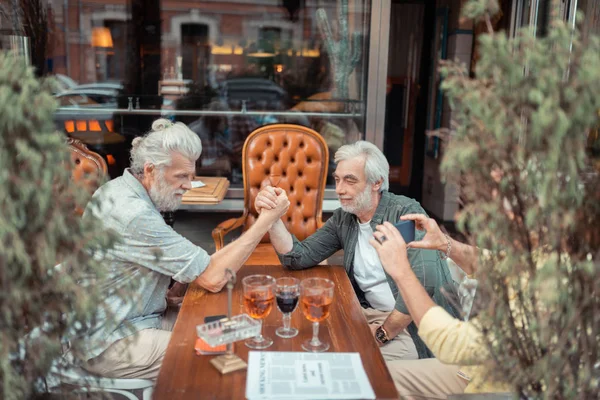 Men arm-wrestling after drinking alcohol outside pub