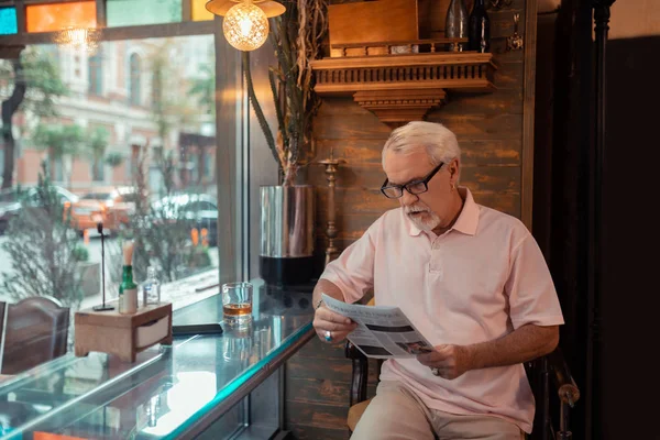 У віці сіроокий чоловік читає новини в пабі — стокове фото