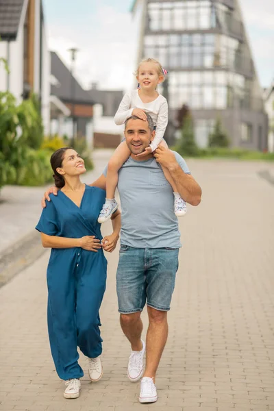 Strong loving man hugging his wife and having daughter on neck — Stock Photo, Image