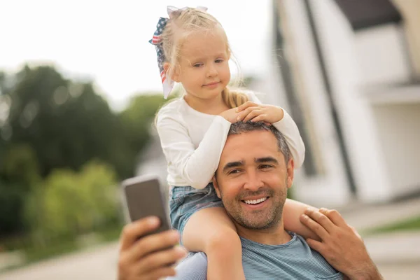 Menina bonito olhando para a câmera enquanto o pai fazendo selfie — Fotografia de Stock