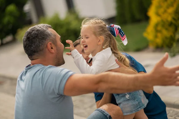 Cute blonde girl making funny face while hugging parents