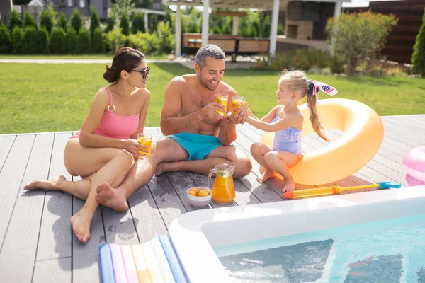 Family drinking refreshing cold juice while sunbathing near pool