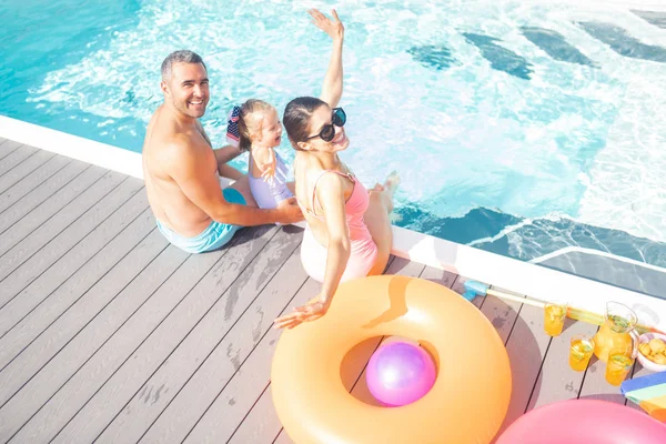 Padres e hija sintiéndose alegres descansando cerca de la piscina — Foto de Stock