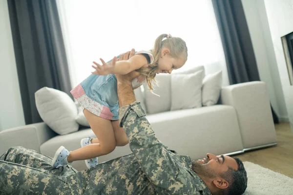 Militaire man liggend op de vloer en het opheffen van zijn schattige mooie dochter — Stockfoto