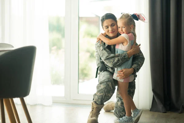 Mörkhårig militär kvinna kramar söt blåögda dotter — Stockfoto