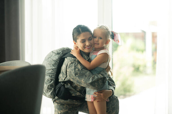 Military woman wearing backpack hugging her lovely girl