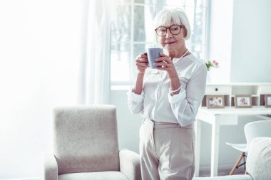 Zarif yaşlı bayan pencere yakınında duran iş kıyafetleri giyiyor