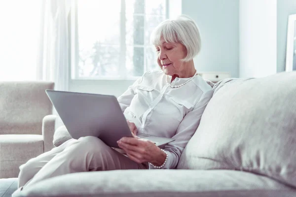 现代退休妇女拿着银色笔记本电脑,而观看视频 — 图库照片