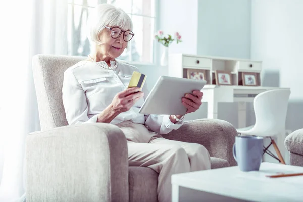 Modern pensionerad kvinna innehar bankkort när du handlar på nätet via Tablet — Stockfoto