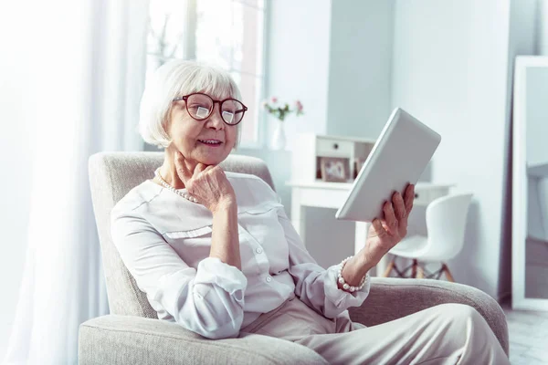 Beaming elegante mujer jubilada sosteniendo la tableta mientras mira fotos familiares — Foto de Stock