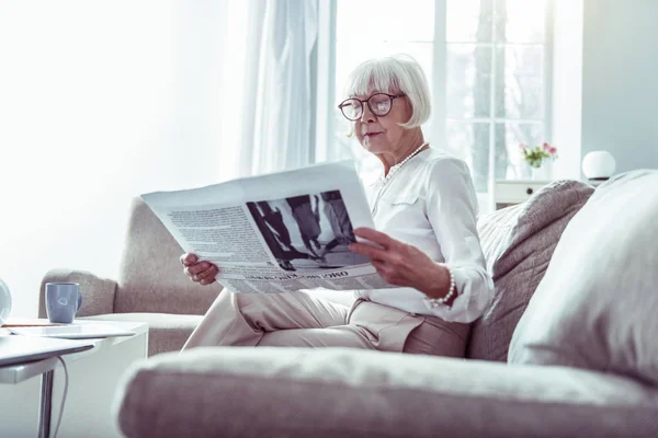 Gyönyörű idős nő olvasatban újság várakozás közben a férj otthon — Stock Fotó