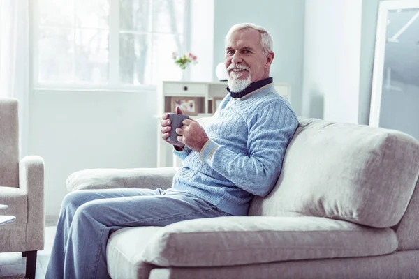 Un hombre retirado radiante con jeans y suéter azul bebiendo té — Foto de Stock