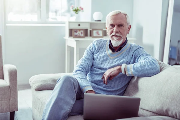 Niebiesko-oczach Brodaty emerytowany człowiek siedzi w jasnym przytulnym salonie — Zdjęcie stockowe