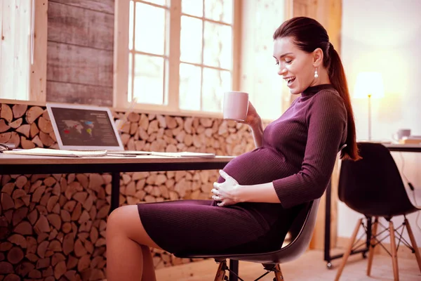 Счастливая беременная девушка сидит на своем рабочем месте — стоковое фото