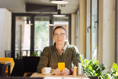 Olumlu bir gülümseme. Yakışıklı çekici adam elinde akıllı telefon ile masada otururken size bakıyor