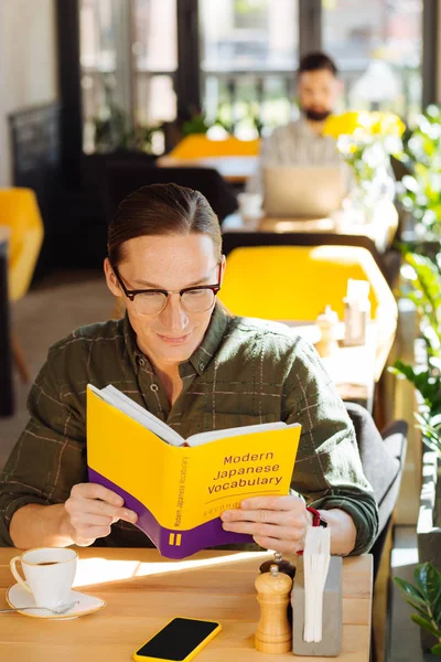 Knowing Japanese. Positive good looking man smiling while enjoying studying new languages