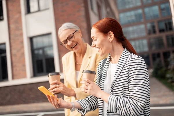 Great mood. Waist-up of two contented friends in stylish clothes laughing outdoors in front of an office building