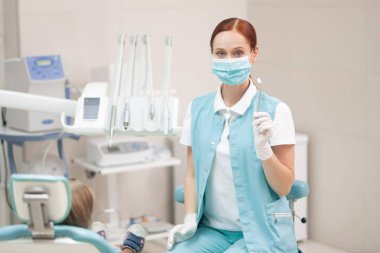 Üniforma ve maske takan kızıl saçlı çocuk diş hekimi