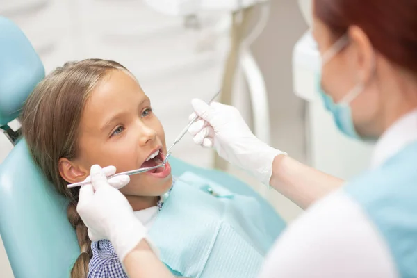 Dentista criança experiente examinando bonito estudante loira — Fotografia de Stock