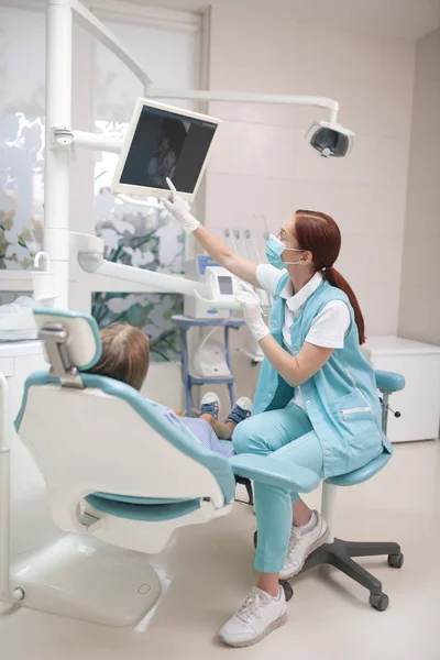 Red-haired child dentist showing the X-ray on screen to girl — Stock Photo, Image