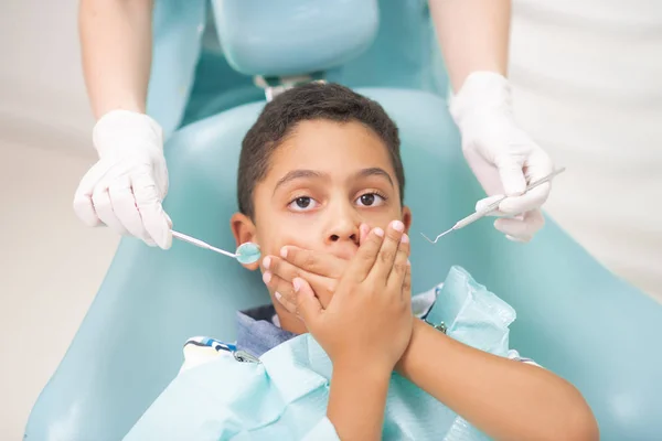 Menino de olhos escuros fechando a boca enquanto se sente com medo do dentista — Fotografia de Stock