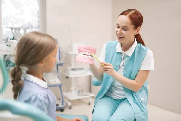 Flicka lyssnar uppmärksamt på tandläkare lära henne att borsta tänderna ordentligt — Stockfoto