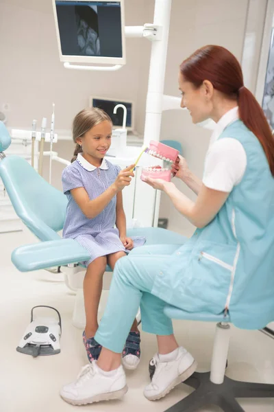 Rothaarige Kinderzahnärztin lehrt Mädchen, Zahnbürste zu benutzen — Stockfoto