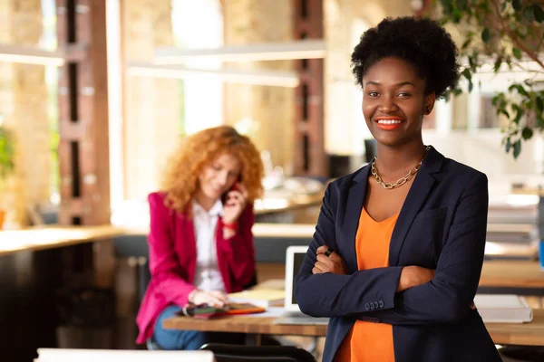 Curly dark-skinned office worker standing near table