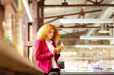 Pencerenin yanında duran ve telefonu kullanan ofis çalışanı