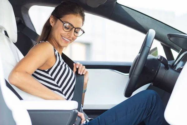 Woman wearing glasses sitting in her car and fastening seat belt — Stock Photo, Image