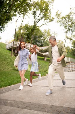 Parkta ebeveynleri ile yürürken sevimli kız atlama