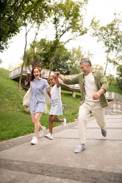 Милая девушка прыгает во время прогулки с родителями в парке
