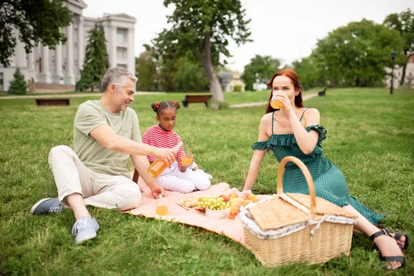 Hija sintiéndose alegre mientras hace un picnic con padres adoptivos — Foto de Stock