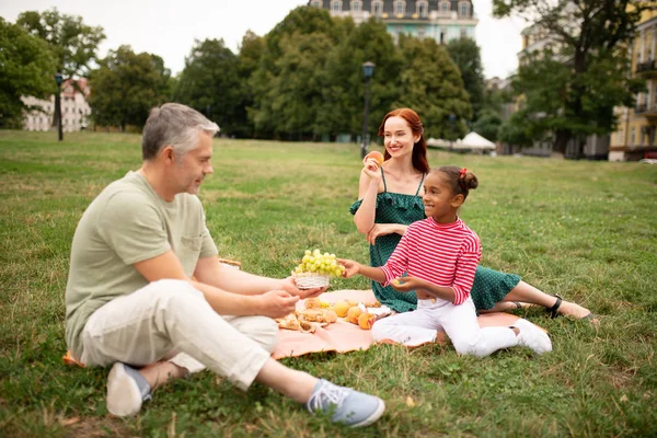 Chica tomando uvas durante el picnic con los padres — Foto de Stock