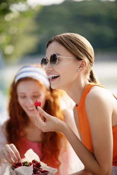 Vacker kvinna i solglasögon leende medan du äter jordgubb — Stockfoto