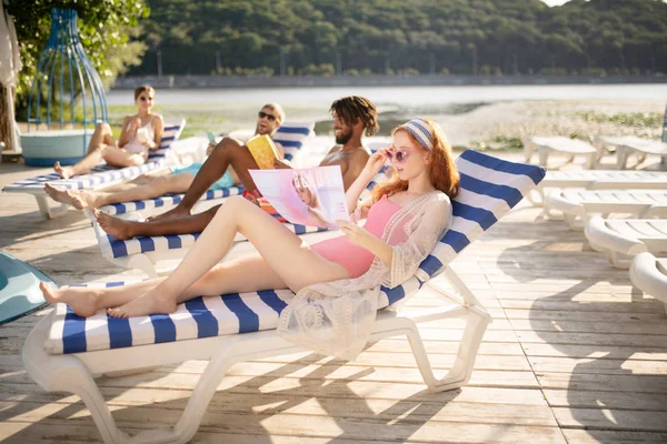 Woman reading magazine while sunbathing with friends