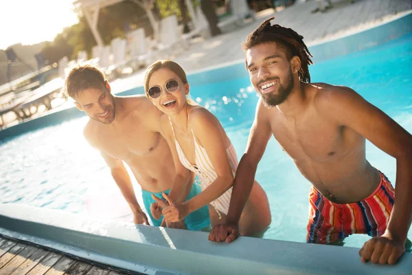 Hombre radiante de piel oscura de pie cerca de amigos en la piscina — Foto de Stock