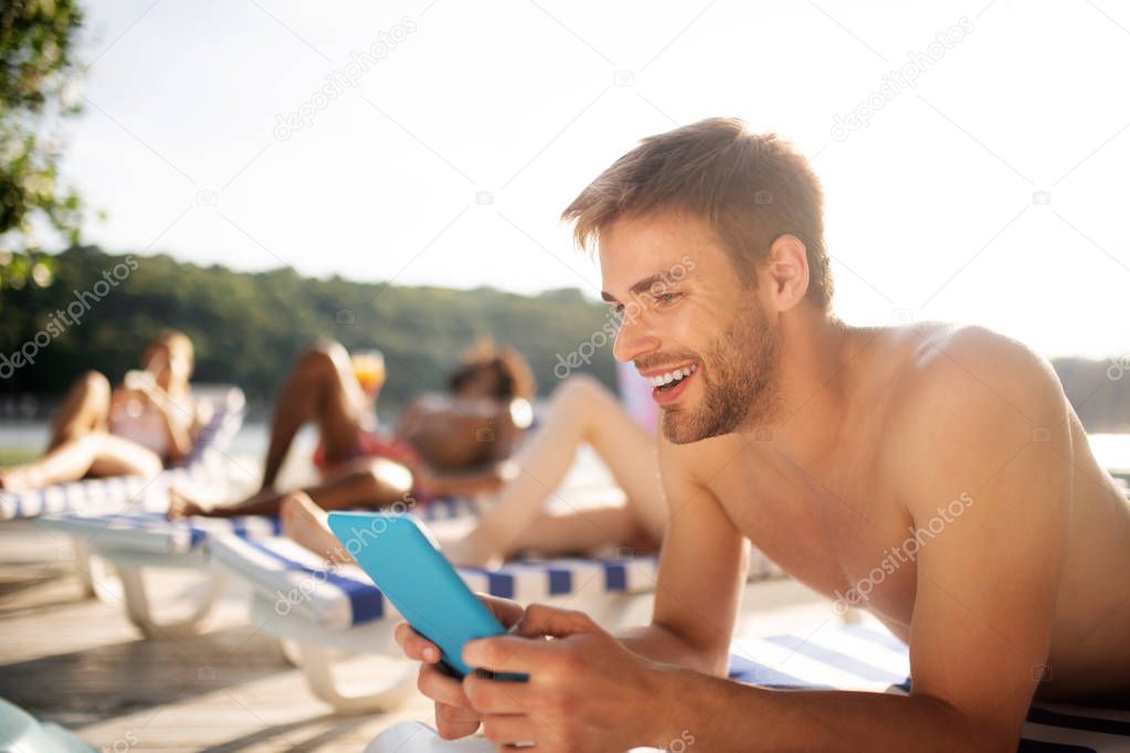 Handsome dark-haired man smiling while watching video on tablet