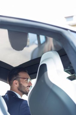 Sakallı genç işadamı araba sürerken gülümsüyor