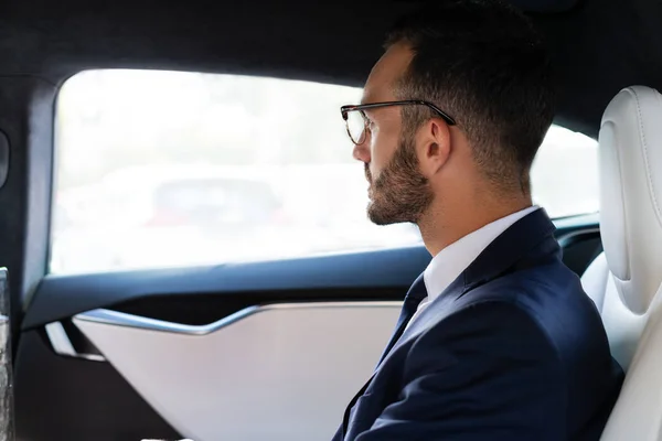Bearded businessman looking into mirror while sitting on back seat — Stock Photo, Image