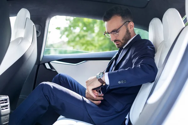 Bearded businessman fastening seat belt while sitting on back seat — Stock Photo, Image