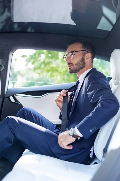 Mladý elegantní muž upevňující bezpečnostní pásy při sezení na zadním sedadle — Stock fotografie